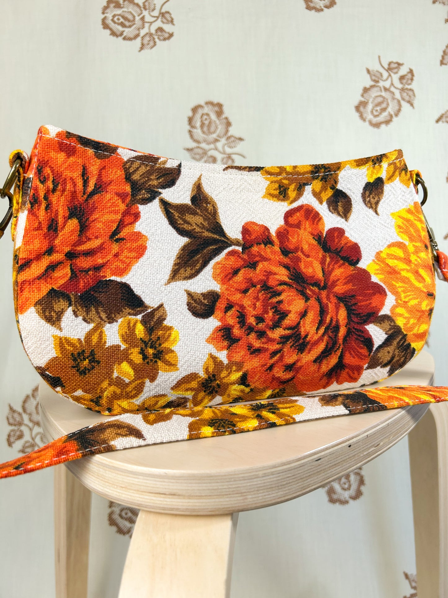 Orange, brown and yellow floral-patterned handbag on a white stool against a floral backdrop