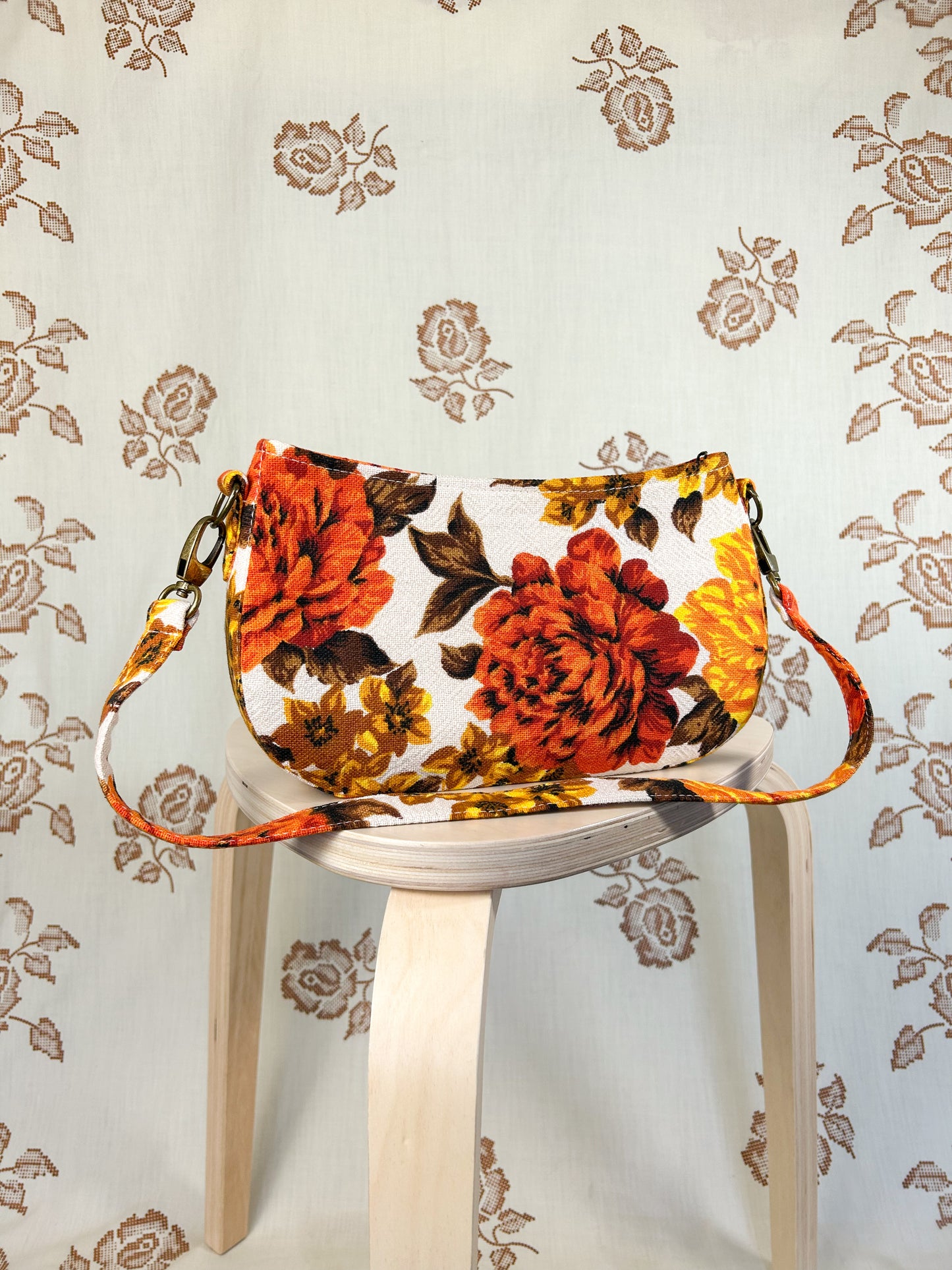 Orange, brown and yellow floral-patterned handbag on a white stool against a floral backdrop