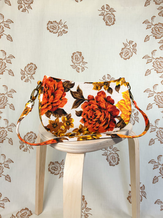 Orange, brown and yellow floral-patterned handbag on a white stool against a floral backdrop