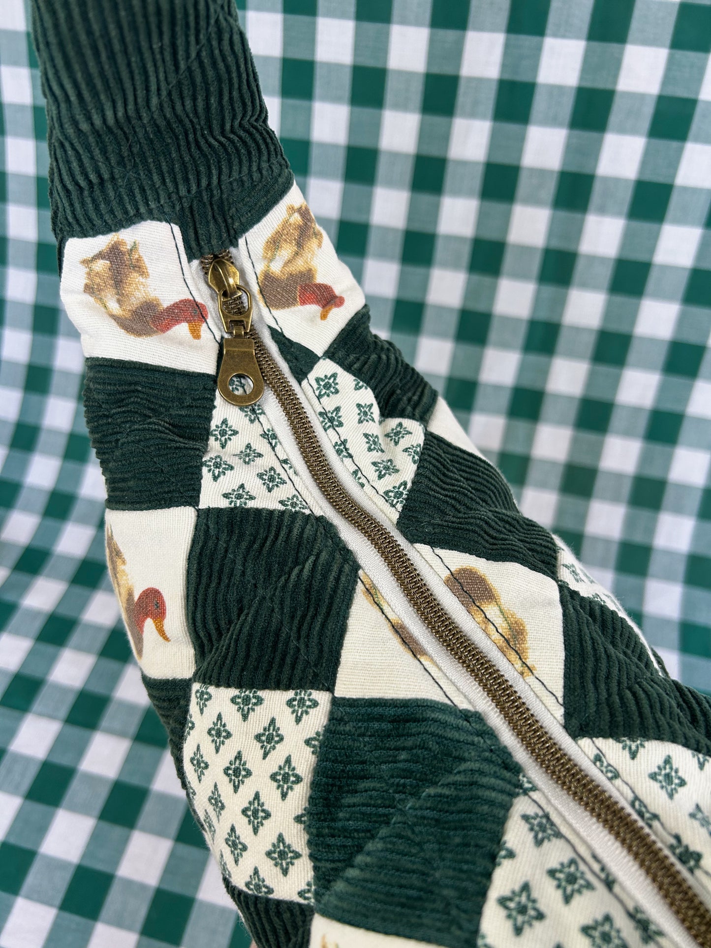 Top view of the same crescent bag showing the antique brass nylon coil zipper in front of a green and white gingham backdrop