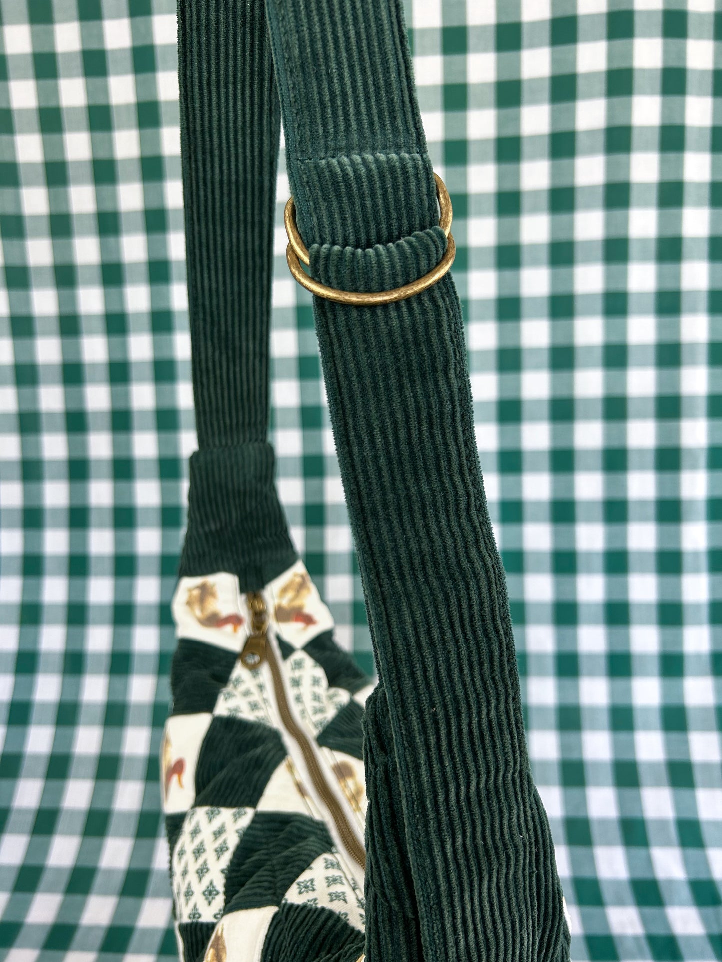 Green corduroy strap with d ring adjuster for the same crescent bag in front of a green and white gingham backdrop