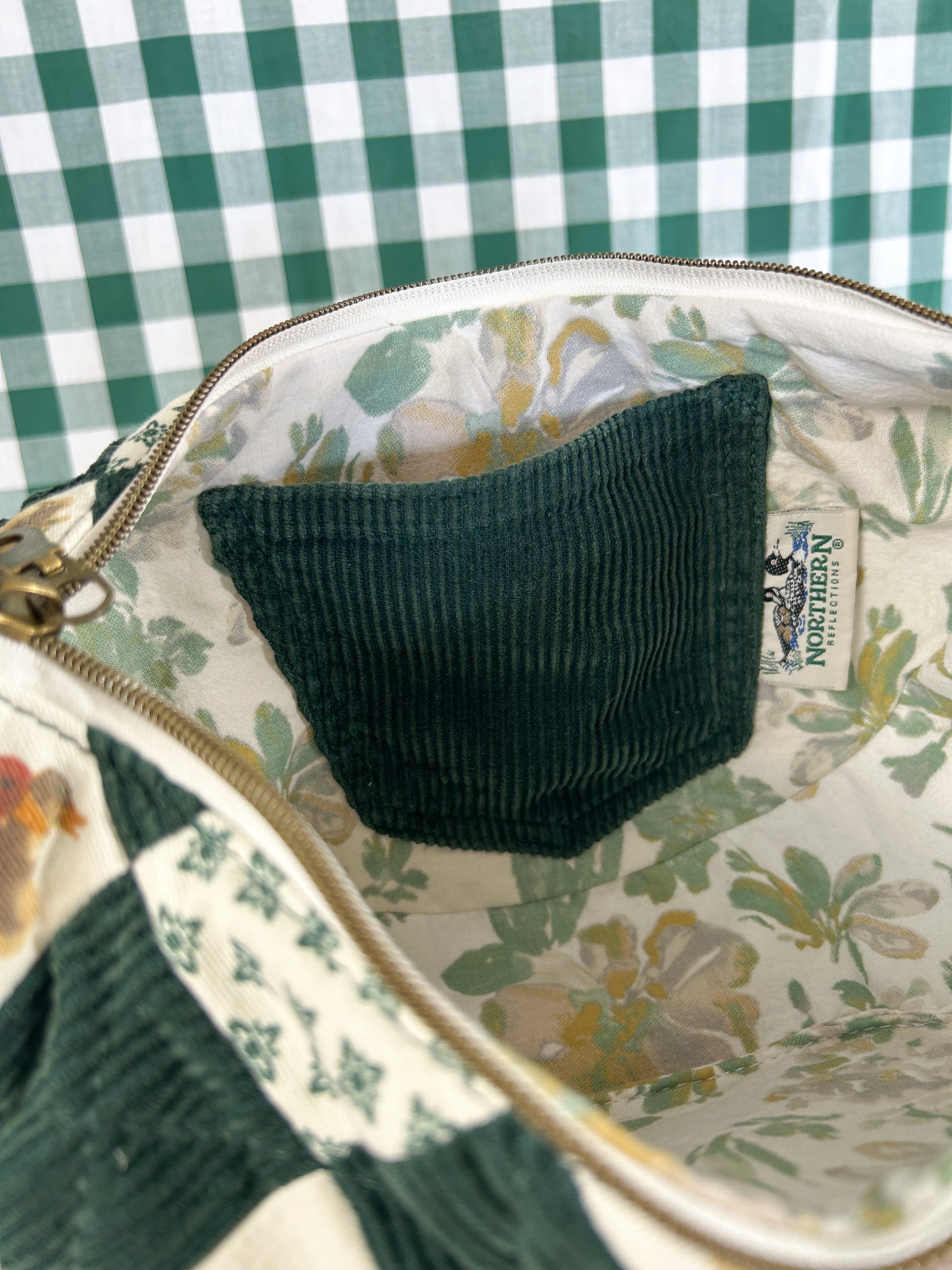 Green interior slip pocket on the inside of the bag with a vintage Northern Reflections tag and floral lining in front of a green and white gingham backdrop