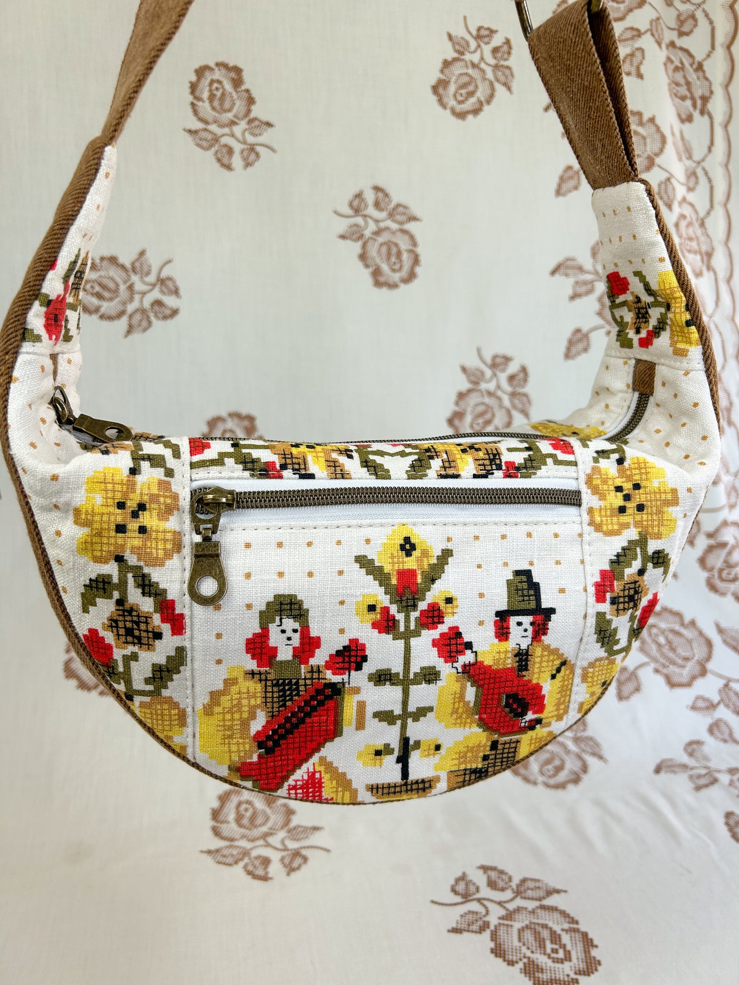 Close up of the same bag showing the front of the bag and its zippered pocket in front of a light cream coloured floral backdrop