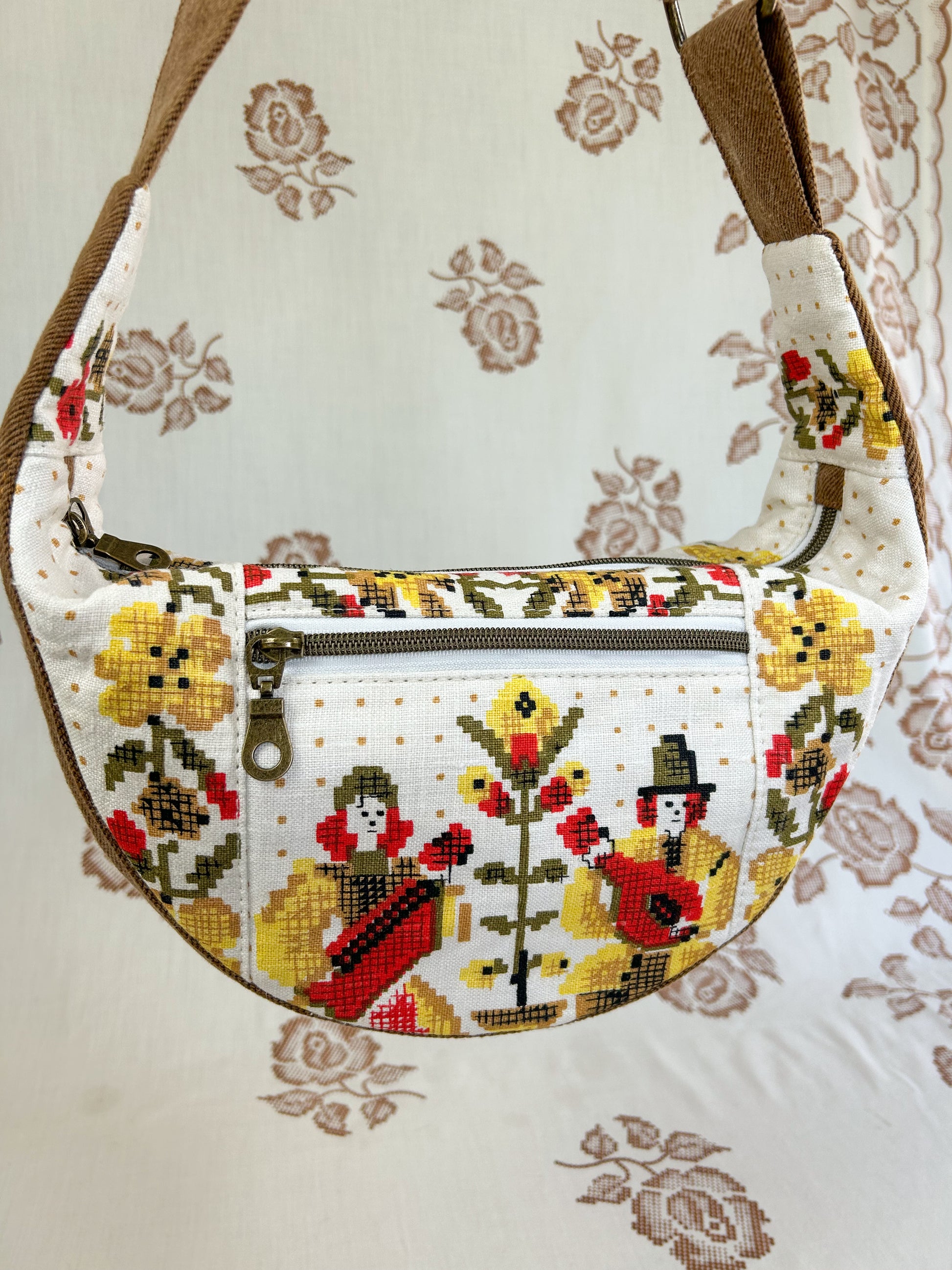Close up of the same bag showing the front of the bag and its zippered pocket in front of a light cream coloured floral backdrop