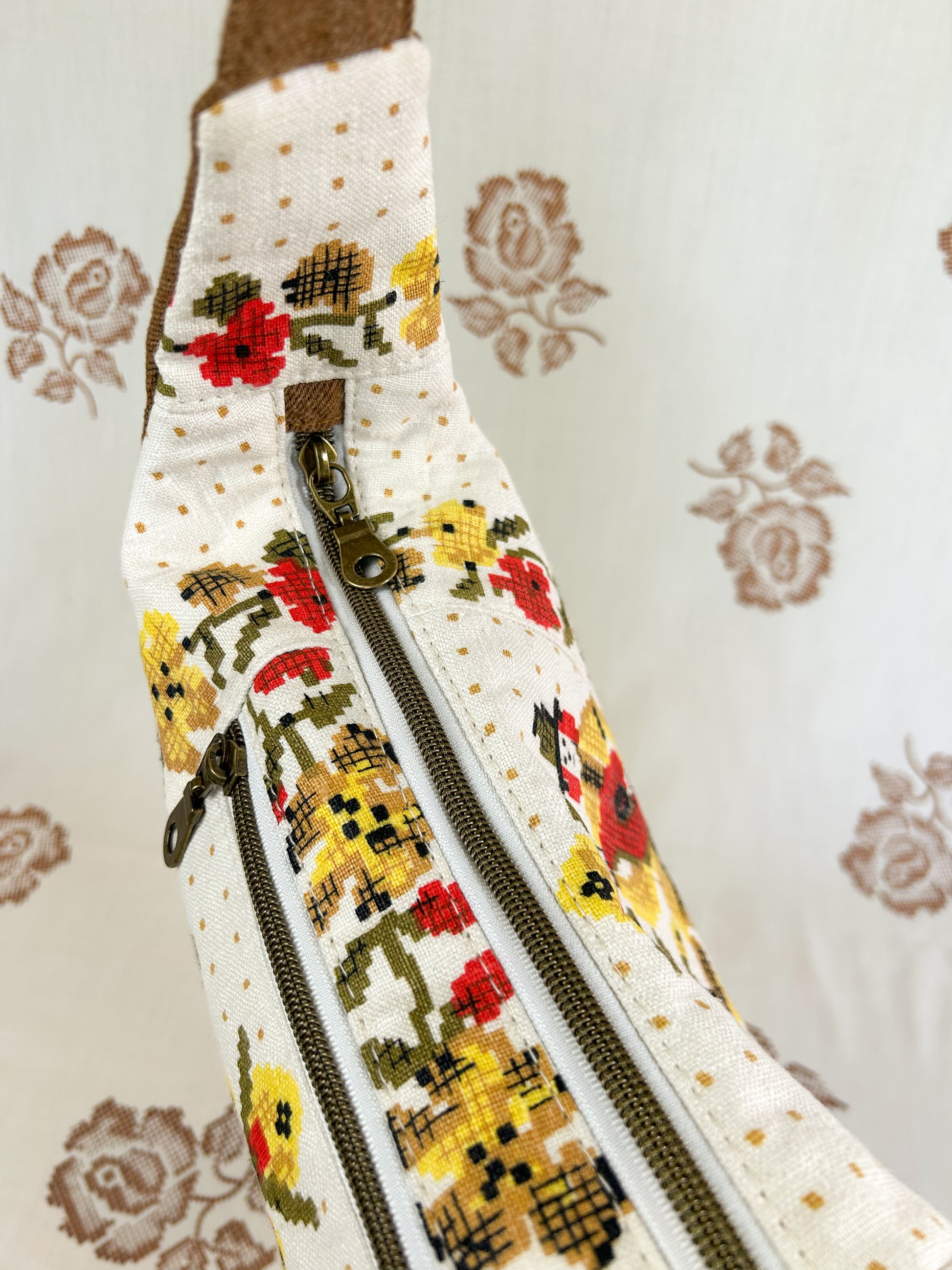 Top view of the same bag showing the antique brass nylon coil zipper in front of a light cream coloured floral backdrop