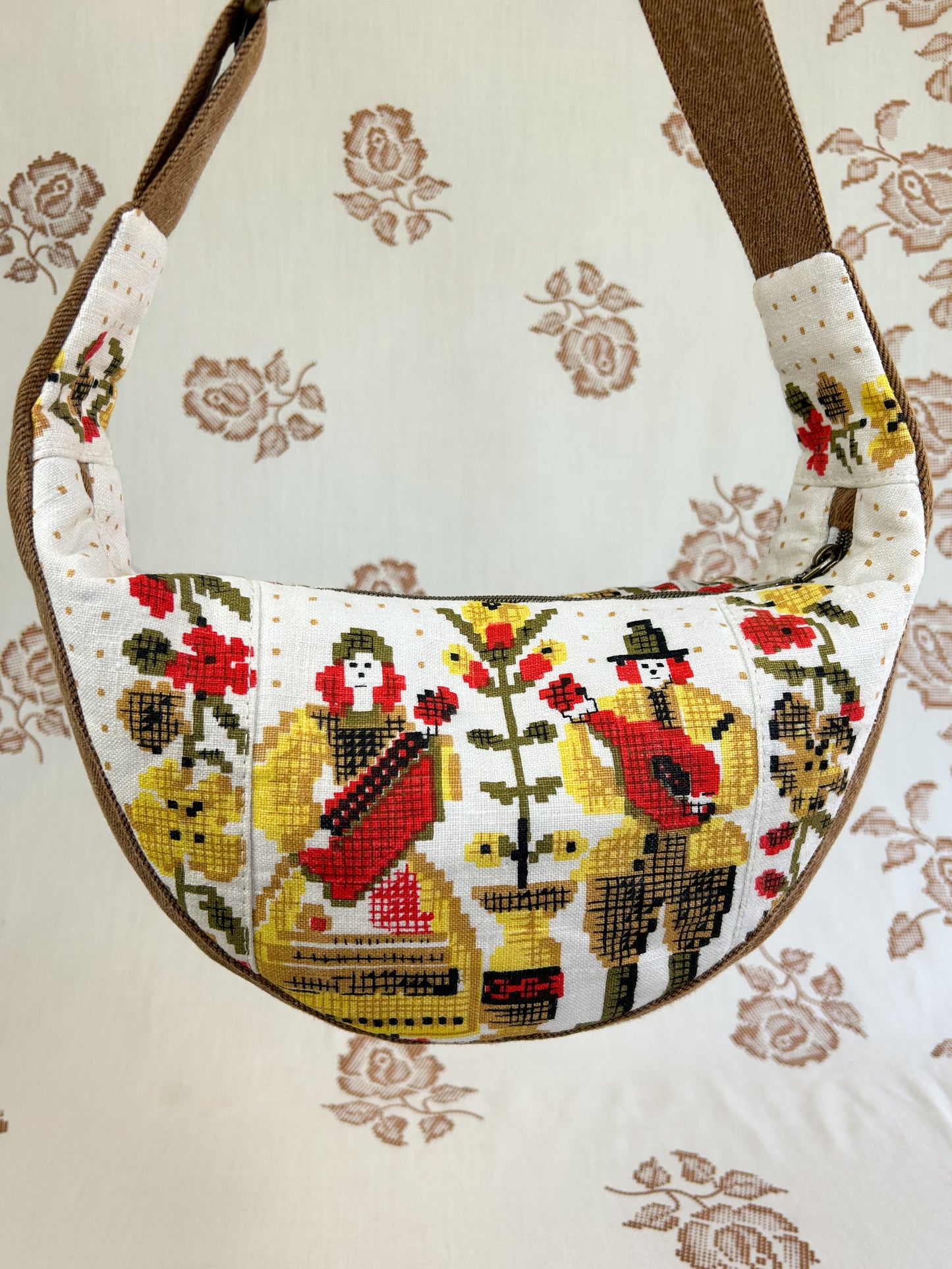 Close up of the same bag showing the back side of the bag with the musican and floral print in front of a light cream coloured floral backdrop