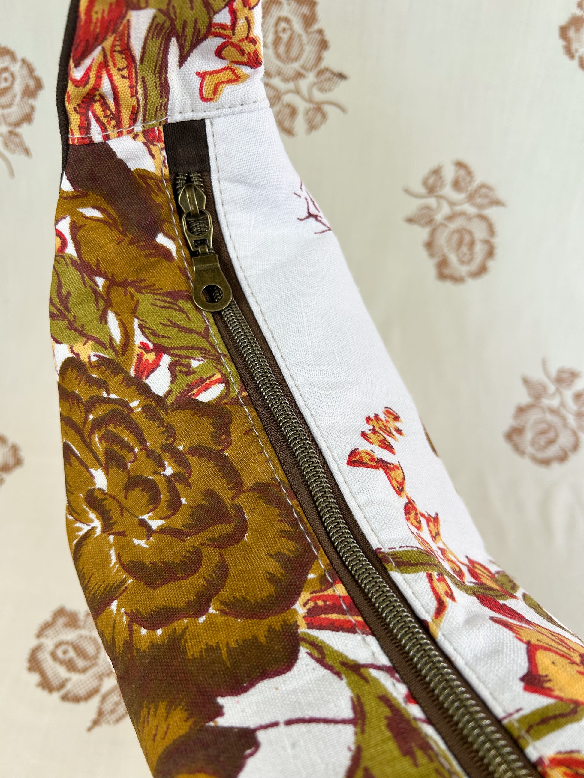 Top view of the same bag showing the antique brass nylon coil zipper in front of a light cream coloured floral backdrop