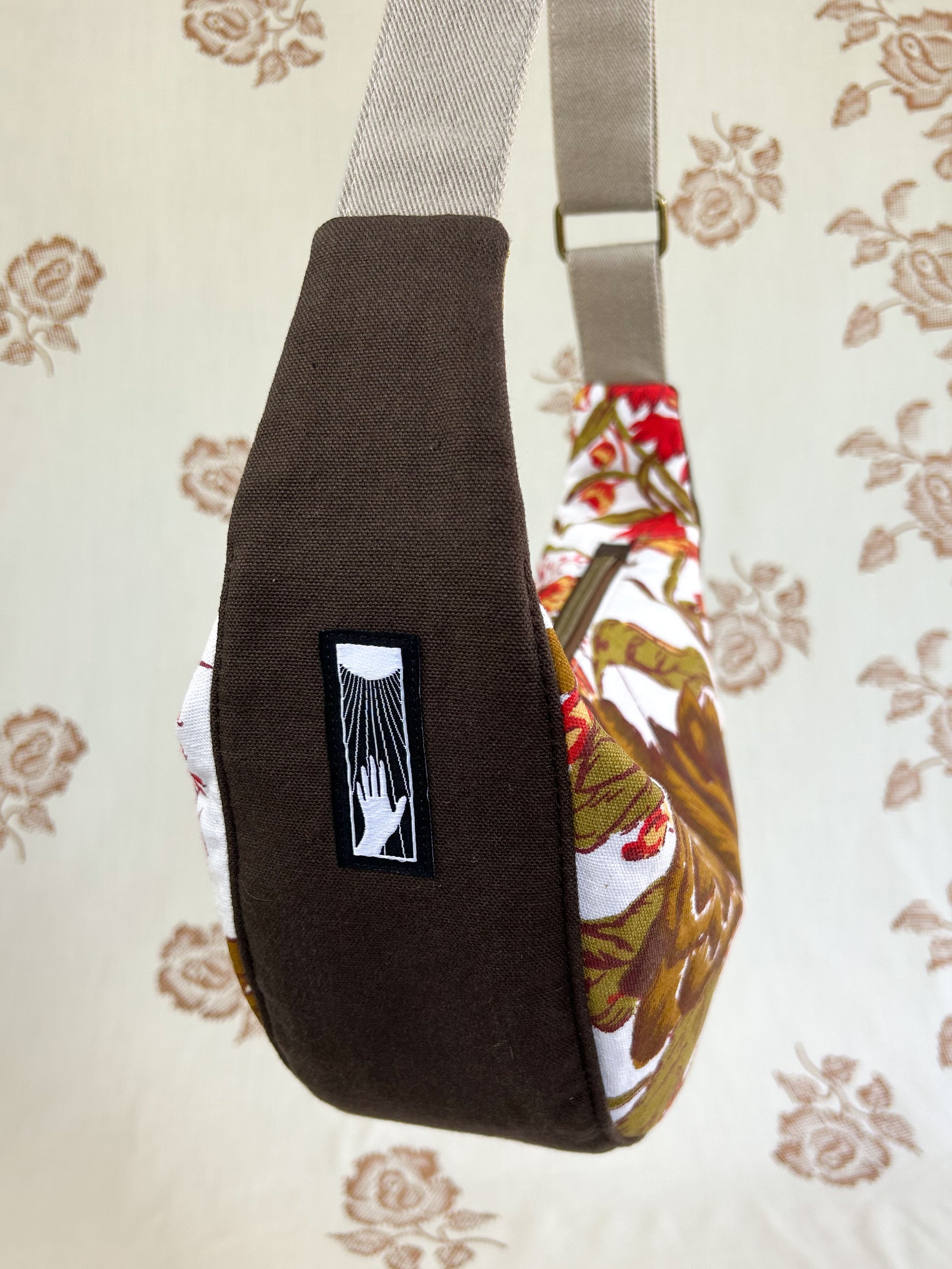 Close up of the side of the bag showing the brown canvas bottom and side piece in front of a light cream coloured floral backdrop
