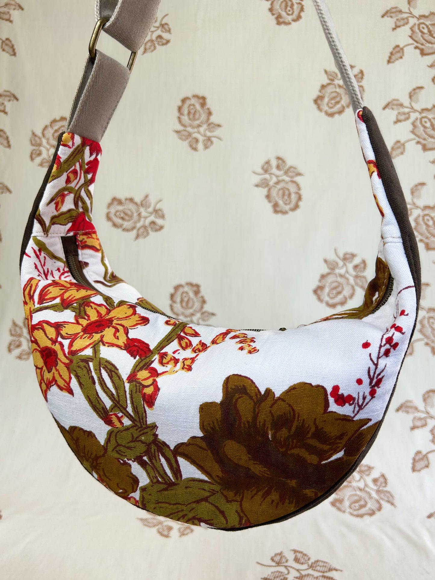 Close up of the same bag showing the floral pattern on the back hanging in front of a light cream coloured floral backdrop