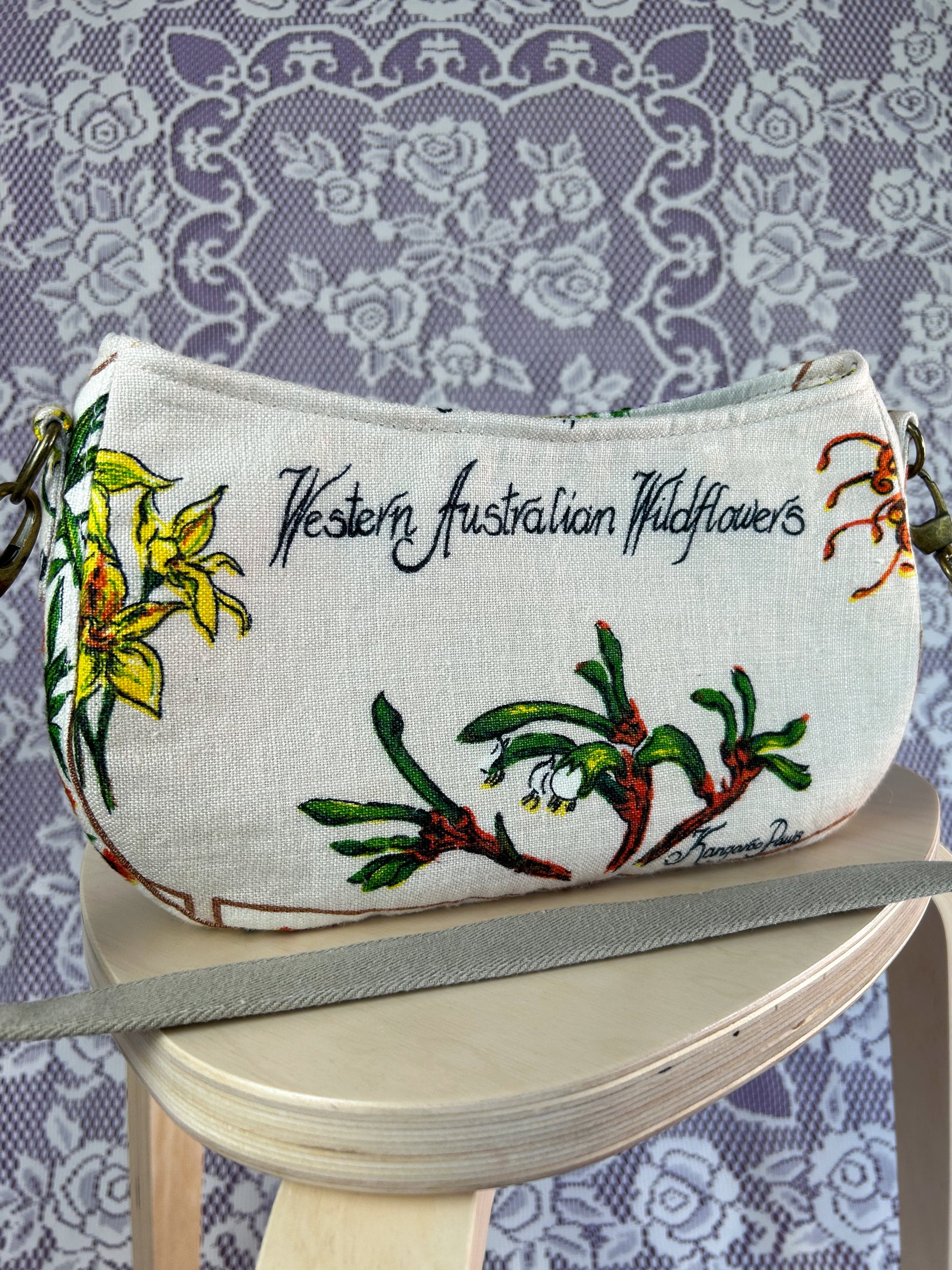 Closeup of the back side of the bag with Western Australian Wildflowers printed text on a wooden stool against a lace-patterned background