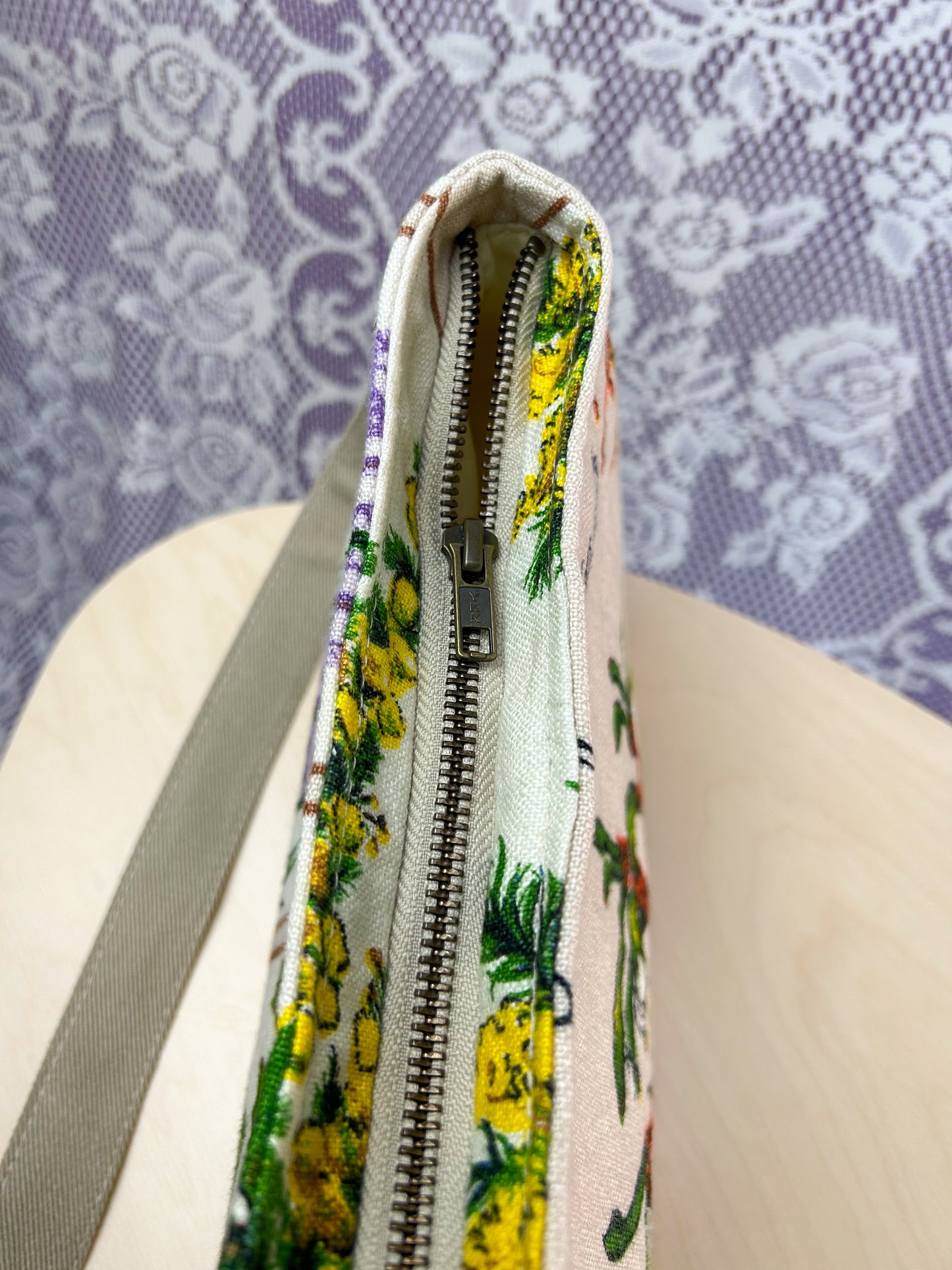 Top view of the handbag showing the antique brass zipper on a wooden stool in front of a lace backdrop