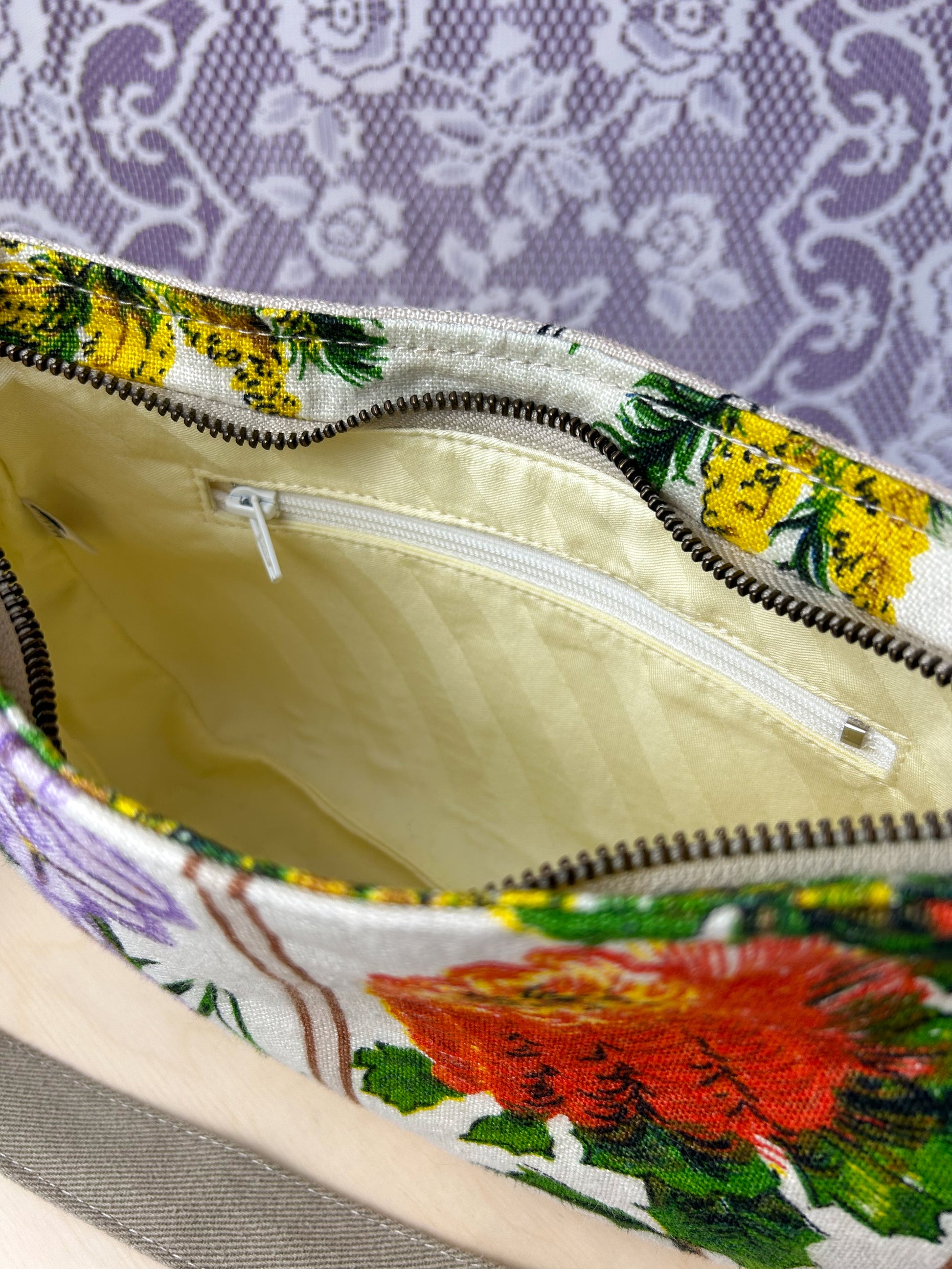Interior view of the handbag showing the cream coloured lining and zippered pocket on a wooden stool in front of a lace backdrop